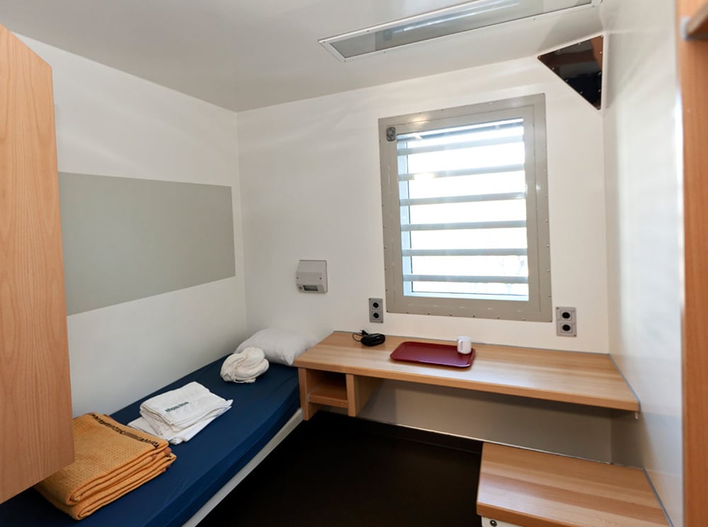 Rum på häktet med säng, skrivbord och fönster.