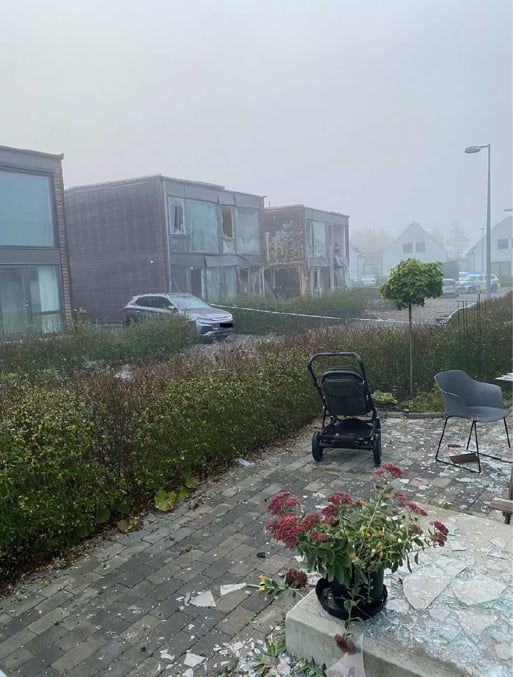 Två hus där fönster och fasader är kraftigt skadade av en explosion. I förgrunden syns en barnvagn och glassplitter.